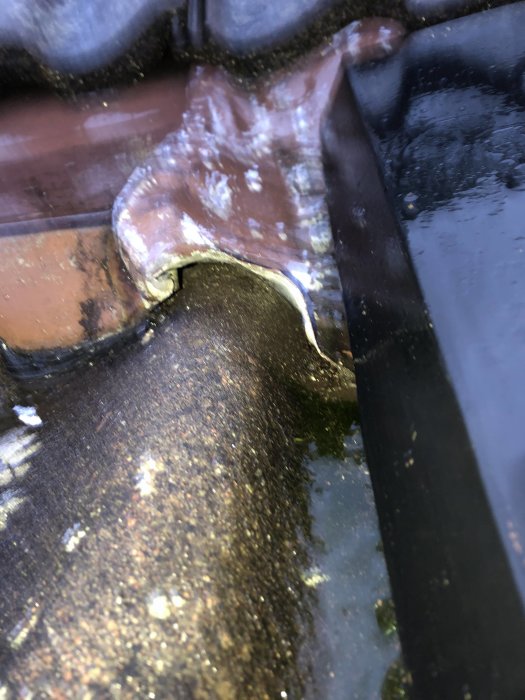 Närbild av takpanna som är förskjuten med synlig metallkantring och vattenansamling.