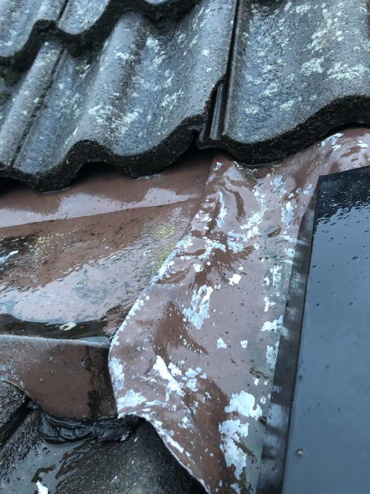 Närbild på tak med betongpannor och plåtdetaljer, viss skada och förflyttning noterbar.