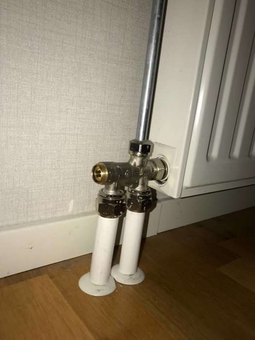 Radiatoranslutning med termostatventil och två vita rör som kommer upp från golvet.