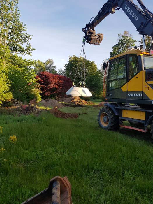 Grävmaskin från Volvo som arbetar med markarbete och avlopp i en trädgård.