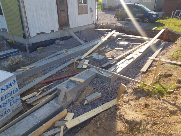 Pågående byggarbete med formar och armering klar för gjutning av grund till framtida trädäck, vid en husgavel under renovering.