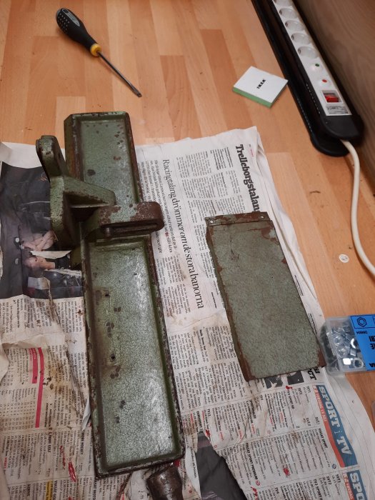 Demonterat anhåll på tidningspapper med verktyg och skruvar i bakgrunden som illustrerar pågående reparation.