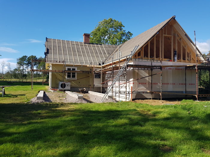 Renovering av ett hus med takbyte från svart plåt till tegelpannor och silvriga plåtdetaljer, omgivet av byggnadsställningar.