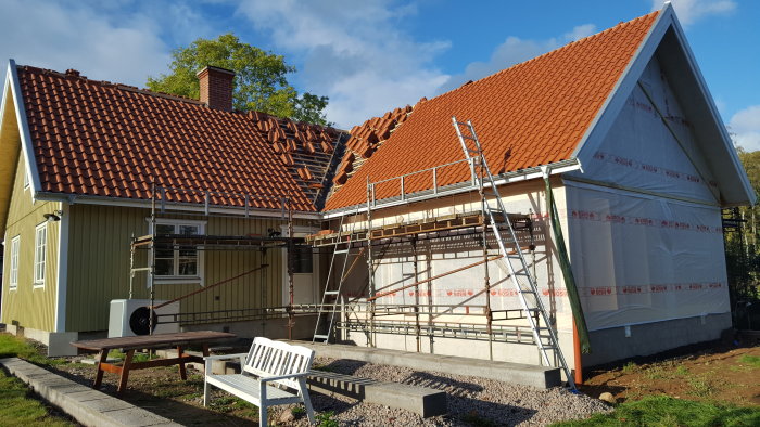 Hus under renovering med nya tegelpannor på taket, ställningar och fasad täckt med byggplast.