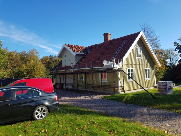 Renovering av grönt hus med nytt tegeltak, ränndal, byggställningar och en röd bil framför.