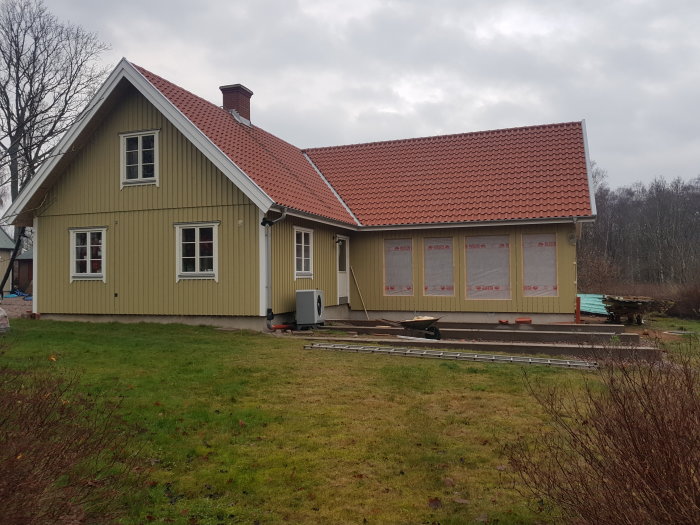 Hus under renovering med nytt tak, målade fasadbrädor och fönster täckta med plastskydd.