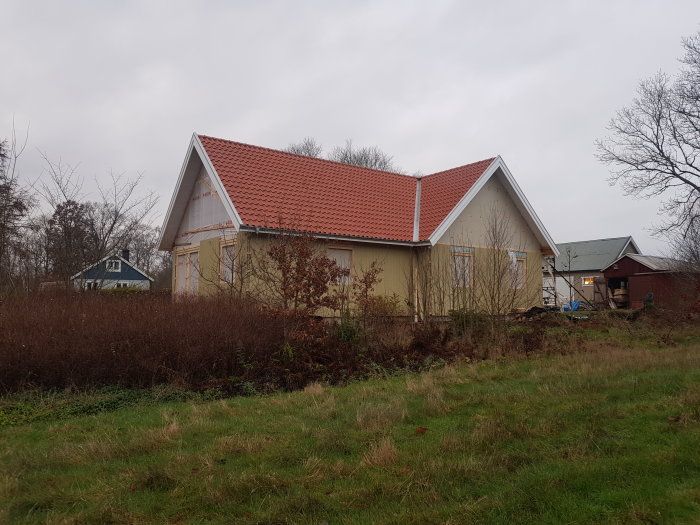 Ett hus under renovering med nytt rött tak, fasad med underbrädor och en hemmabyggd fågelskrämma fäst på sidan.