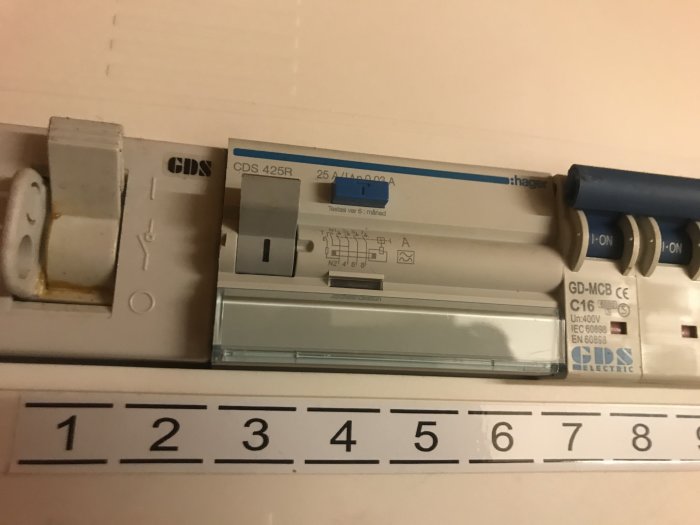 Elektriskt säkerhetsbrytare och en gammal uttag bredvid en mätsticka på en elpanel.