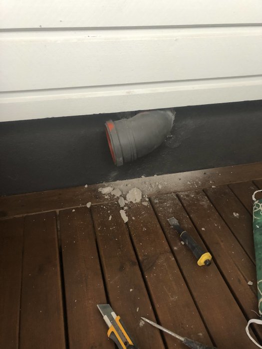 Renoverat ventilationssystem med ett mindre avloppsrör täckt med alutejp installerat i större hål i betongvägg, verktyg på trägolv.