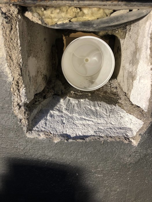 Ventil installerad i fyrkantigt hål i betong med synlig silikon och alutejp runt kanterna.