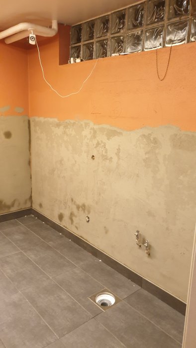 Tvättstuga under renovering med halvt borttagen orange-röd färg och nyputsad vägg.