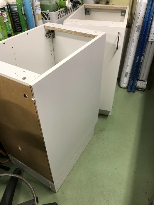 Två vita skåpstommar med synlig sockel, använda som skrivbordsstöd, står i ett verkstadsutrymme.