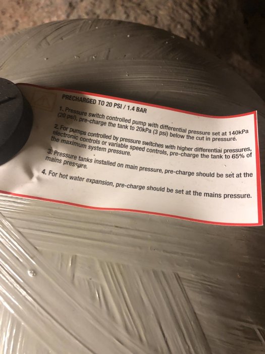 En etikett på ett tryckkärl för bruksvattenpump med instruktioner på engelska, angående förinställt tryck.