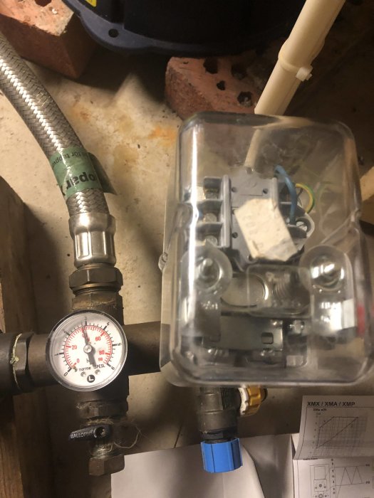 Tryckströmbrytare och manometer i en vatteninstallation, antydan på inställningar för vattentryck.