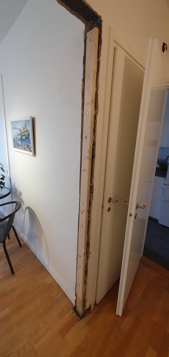 Renoverad vägg där gips tagits bort, visar träreglar, skruvar och limrest, bredvid en vit dörr.
