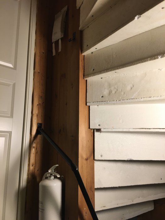 Oisolerad trappa i trapphus med trävägg till vänster och brandsläckare under, behov av renovering och isolering.