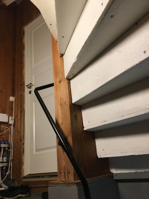 Ofärdigt trapphus med vita trappsteg och en osäkrad sida, träväggar och en vit dörr i bakgrunden.