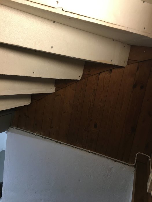Oisolerat trapphus med synliga trappsteg och träpanel, behov av renovering och isolering.