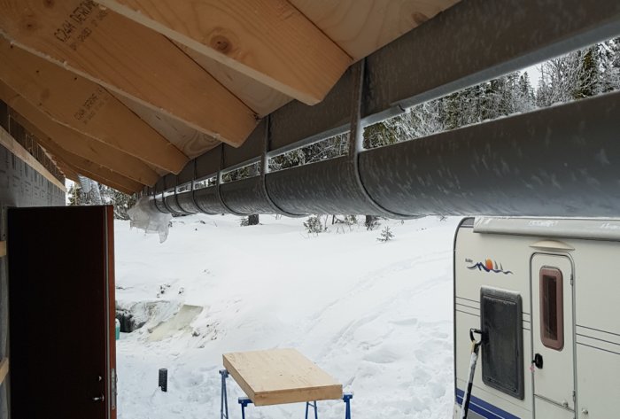 Takutsprång med ränna som blockerar dörröppning på husbygge i snöigt landskap.