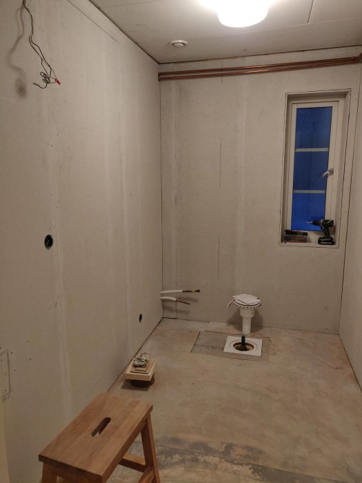 Nyrenoverat rum med fibergipsskivor på väggarna, oslipade skruvkratrar och en toalettstomme i mitten.