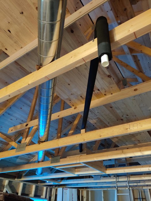 Ett hus under konstruktion med synliga träbjälkar och installation av ventilationssystem och isoleringsmaterial.