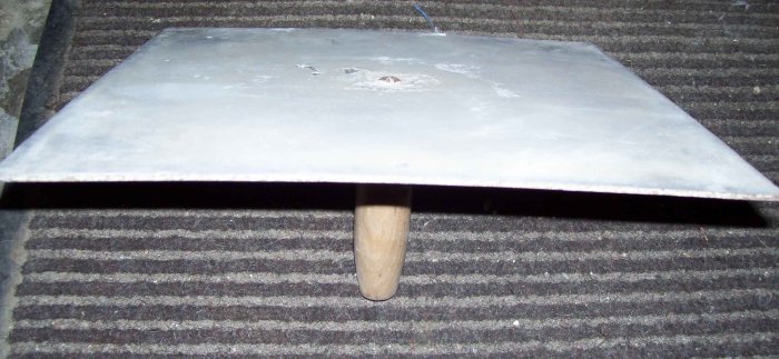 Handgjord skrapa med en platt bit av aluminiumplåt fäst vid ett träkvastskaft, liggande på en trappa.