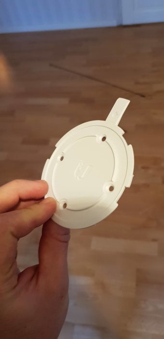 3D-printat fäste för Ubiquiti accesspunkt hållet i en hand mot ett trägolv.