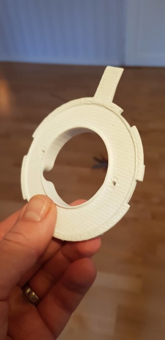 3D-utskrivet vit cirkelformat fäste hålls i handen framför blå bakgrund.