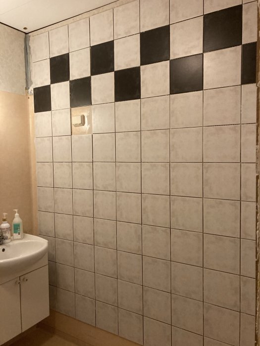 Delvis kaklade väggar med några svarta plattor, utsågat hål för brytare, tvättställ och början på rivning till höger.