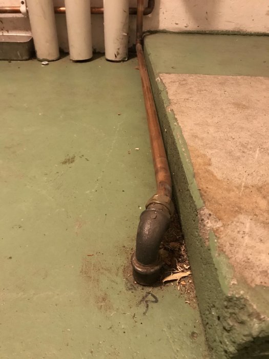 Oisolerad kopparledning märkt med "R" går upp genom källargolvet, omgiven av vita rör och grön betong.