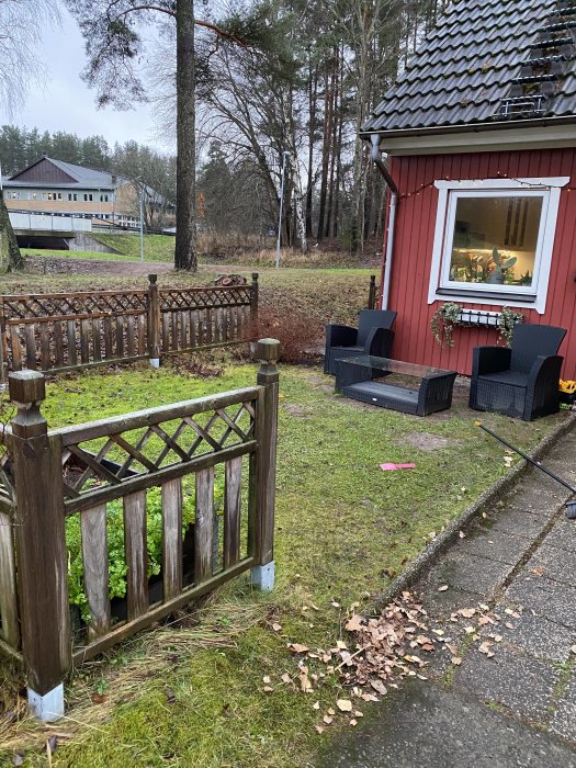 Framsidan av ett rött radhus med en gräsmatta, staket och utemöbler, perfekt plats för ett nytt tralldäck.