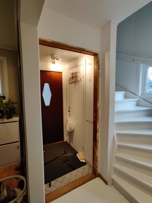 Åbent døråbning uden karm i indgang med værktøj på gulvet og stige til højre, klar til renovering.
