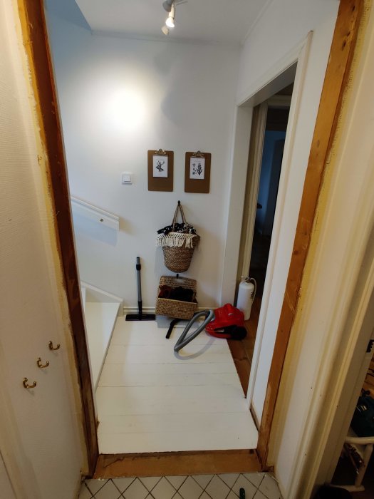 Åbning i en væg efter fjernelse af dørkarm, omgivet af værktøj og rengøringsgenstande; træpaneler og vægudsmykning ses i baggrunden.