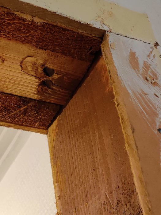 Træregler i en døråbning, hvor karm er fjernet, vises med brunt maling og eksponeret trækonstruktion. Pejse- og vægflader ses tydeligt.