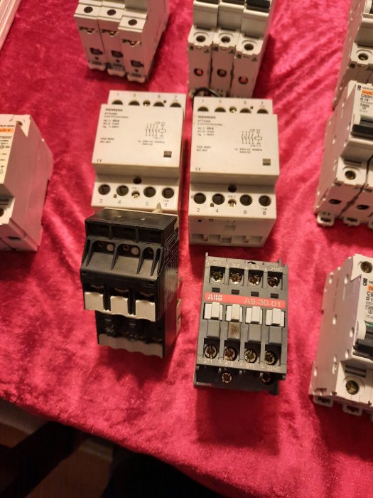 Olika elektriska komponenter såsom automatsäkringar och kontaktorer spridda på ett rött tyg.