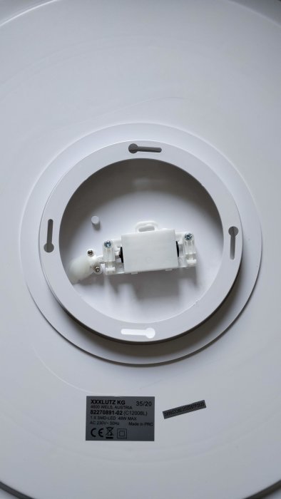 Lampa med vita ringar och centralt fästaggregat för takmontering, etikett från XXXLutz synlig.