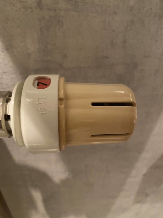 En termostatventil med plastdetaljer som gulnat över tiden, fastsatt på ett värmeelement.