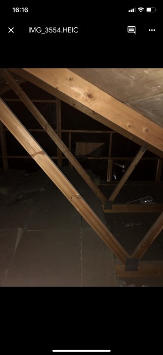 Mörk bild av en takkonstruktion med synliga träbalkar och takstolar inomhus, planer för öppning mot nock diskuteras.