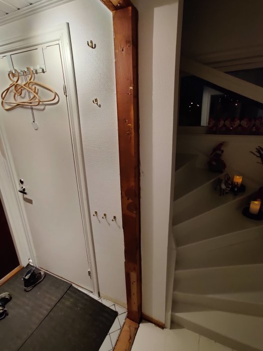 Væg i entre med træramme og kroge; planlægges at skabe en glat væg til opbevaring. Skohorn hænger ved døren, og trin ses til højre.