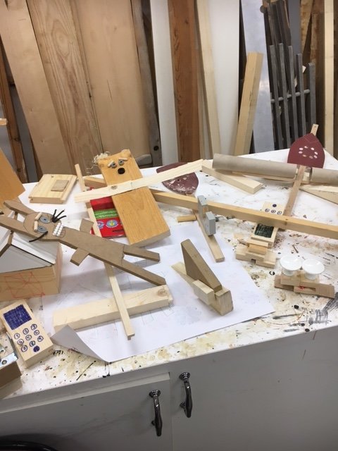 Barnskapade träfigurer med lim och träbitar på en rörig arbetsbänk.