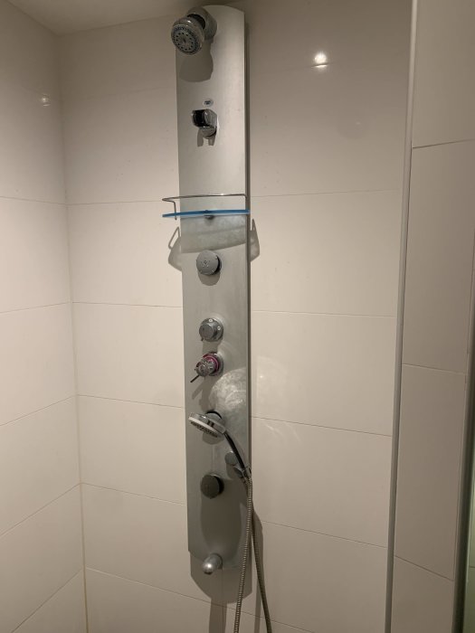 Duschpanel monterad på kakelvägg med synliga rör och olika munstycken, i behov av renovering.