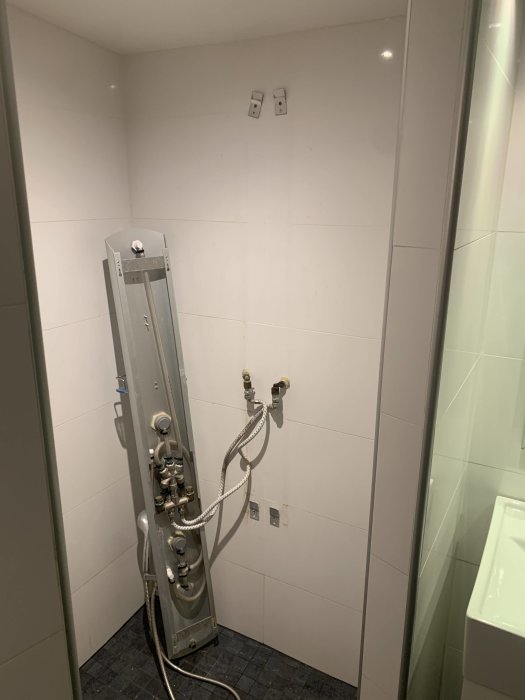 Äldre duschpanel med handdusch monterad på kaklade väggar med synliga rör och eluttag, i behov av renovering.