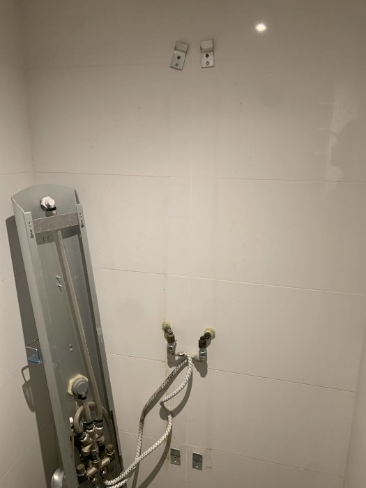 Tak och vägg i badrum med vit kakel och synliga rör samt fästen för gammal dusch.