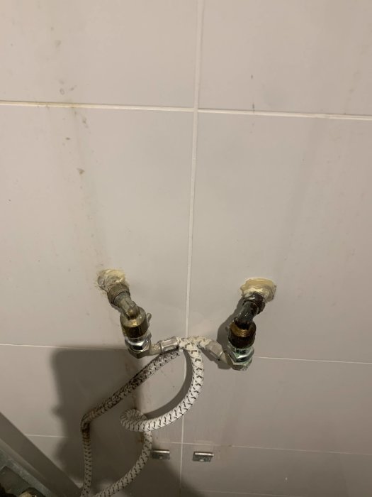 Vägg med kakelplattor och utstickande rör för duschen på en ojämn CC-mått.