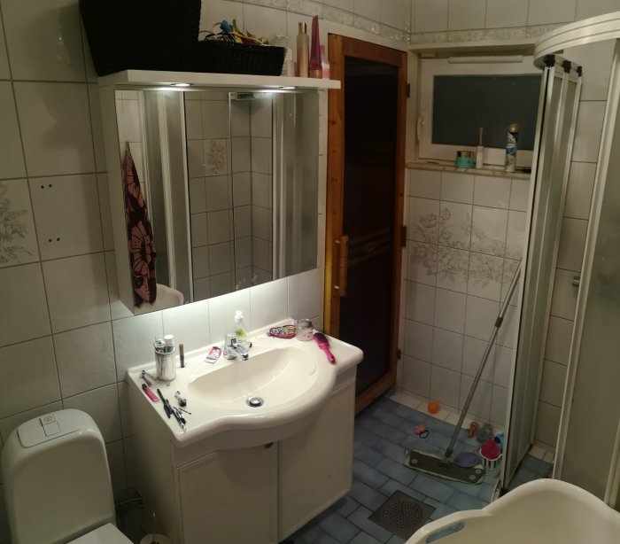 Helkaklat badrum med duschhörn, handfat, toalett och öppen dörr till bastu som ska tas bort under renovering.