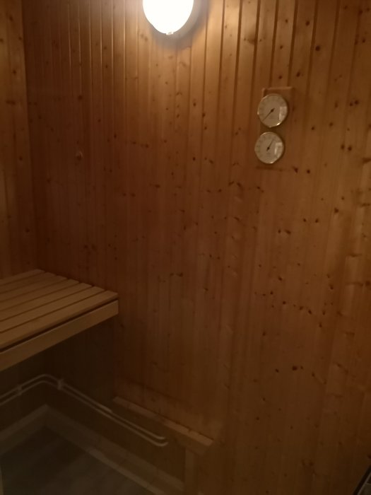 Bastudel av badrum med träpanel på väggar och bänk samt temperatur- och timmätare på väggen.