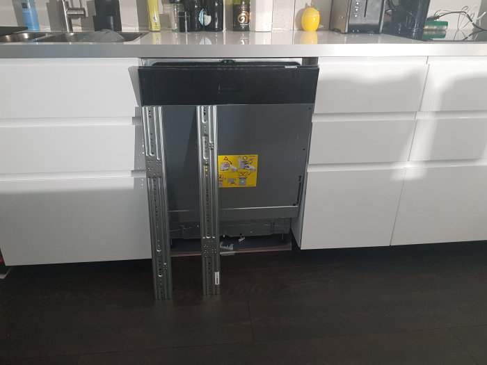 Inbyggd diskmaskin öppen med skenor och utan frontluckor i ett modernt kök.