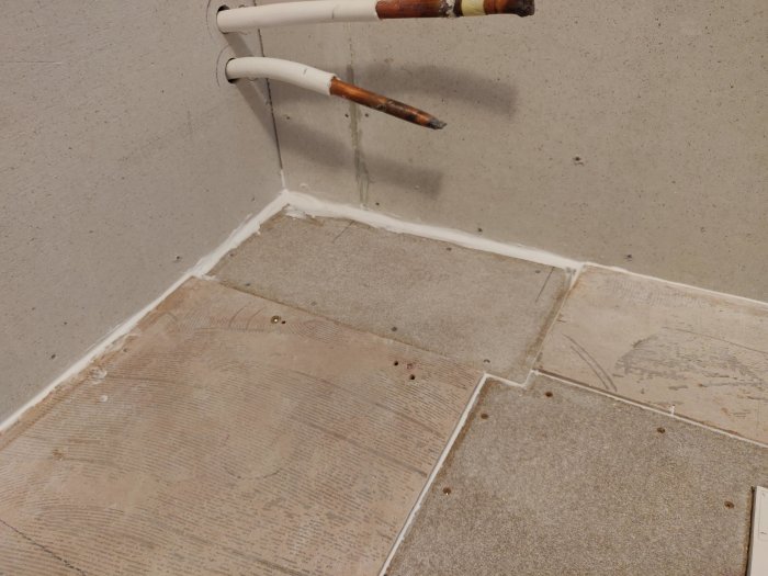 Hörn av ett rum under renovering där Fermacellskivor lagts ned på golvet intill en vägg utan spackelkanter.