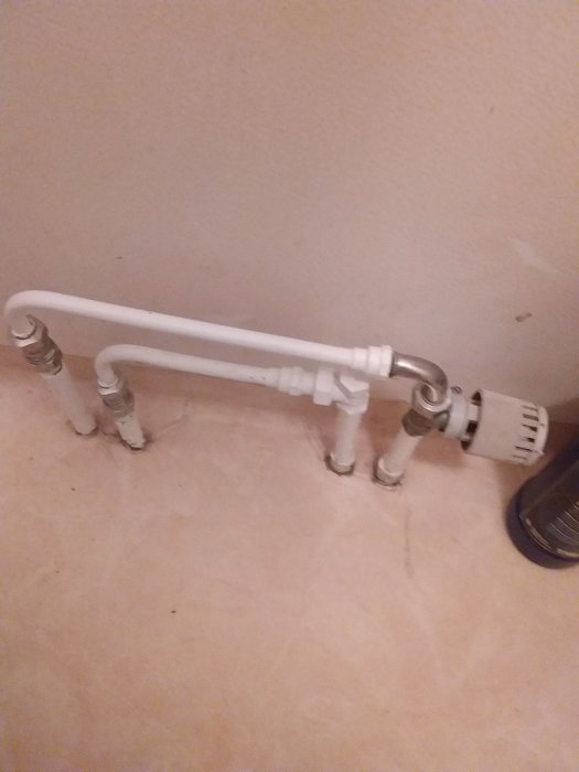Väggmonterad vit radiator med röranslutningar i en liten toalett utan fönster.