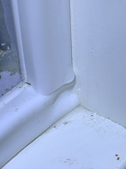 Närbild av ett fönsterhörn med spår av kondens och möjligt vattenskada på fönsterbrädan.